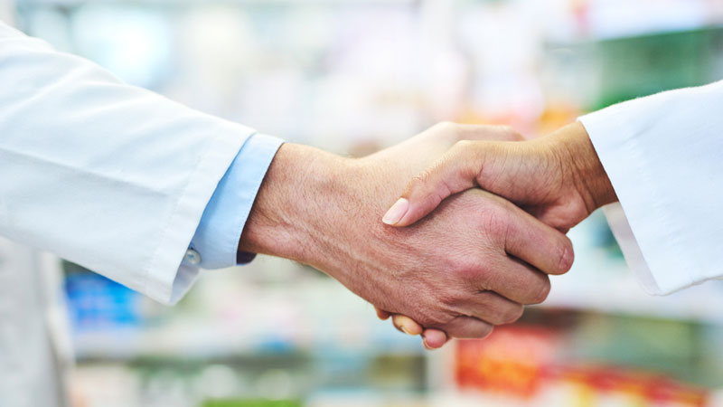 close up of a greeting handshake with pharmacy shelves in the background